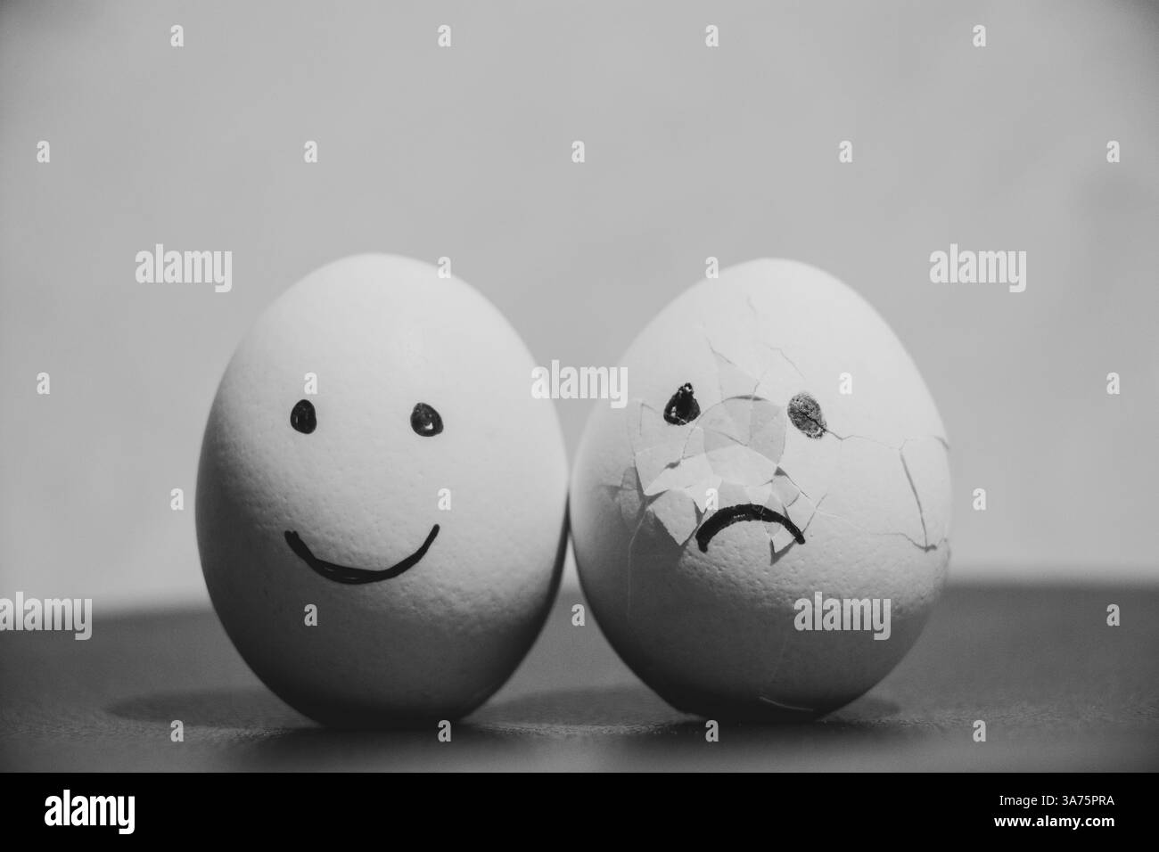 Zwei Hühnereier, eins mit Freude, und das zweite mit traurigen Emotionen auf dem Tisch, Traurigkeit und Trauer Stockfoto Zwei Hühnereier, eins mit Freude, und das zweite mit traurigen Emotionen auf dem Tisch, Traurigkeit und Trauer Stockfoto