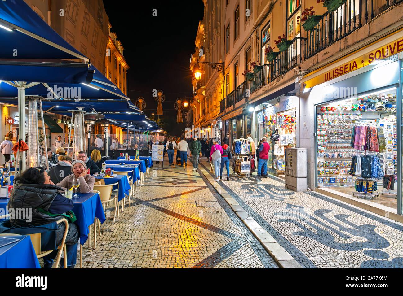 Fußgänger genießen Straßencafés und Geschäfte auf der beleuchteten Straße Rua Augusta mit Lichtern, die nach Regen auf dem Bürgersteig reflektieren, Lissabon Portugal. Stockfoto
