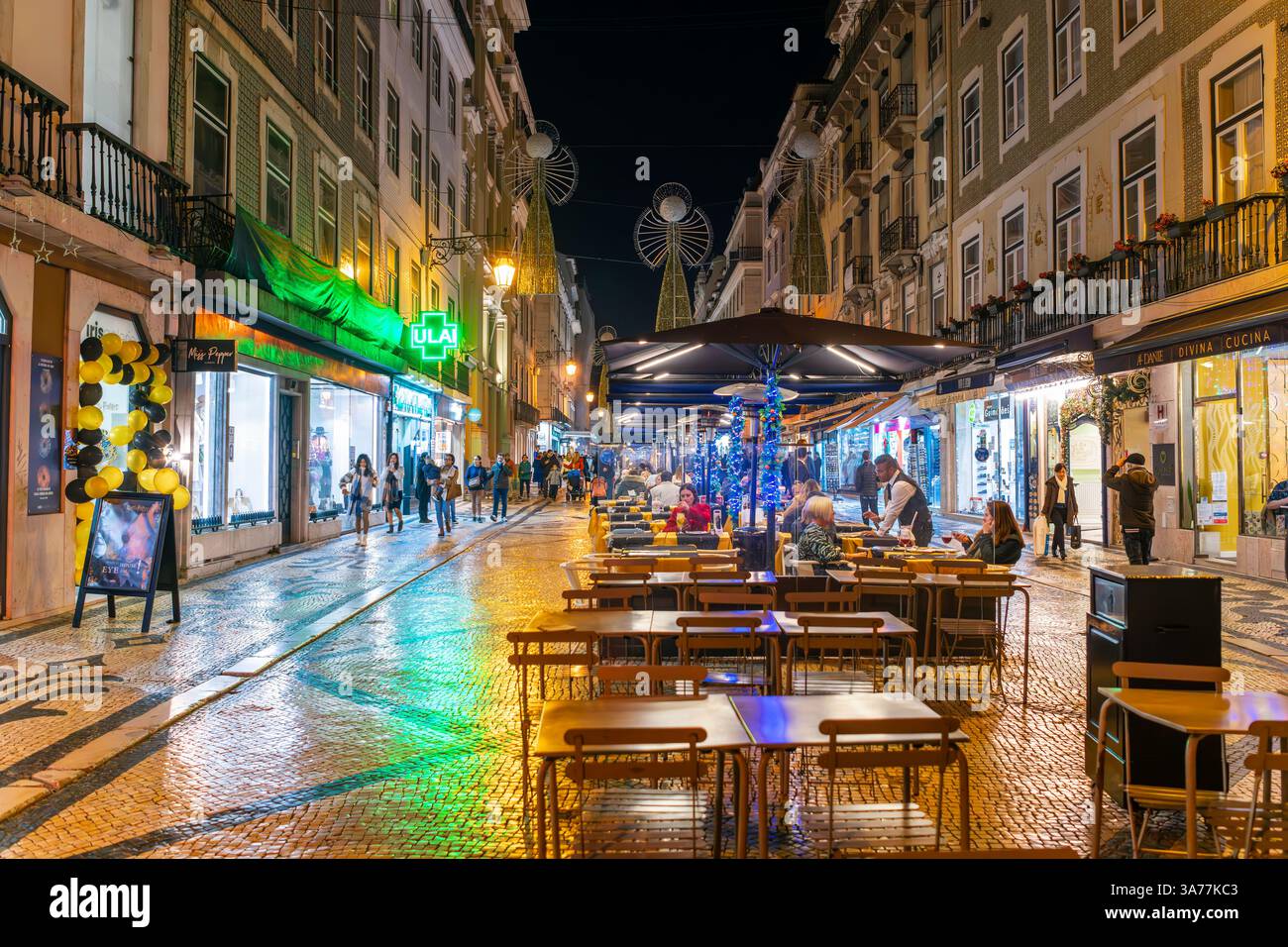 Fußgänger genießen Straßencafés und Geschäfte auf der beleuchteten Straße Rua Augusta mit Lichtern, die nach Regen auf dem Bürgersteig reflektieren, Lissabon Portugal. Stockfoto