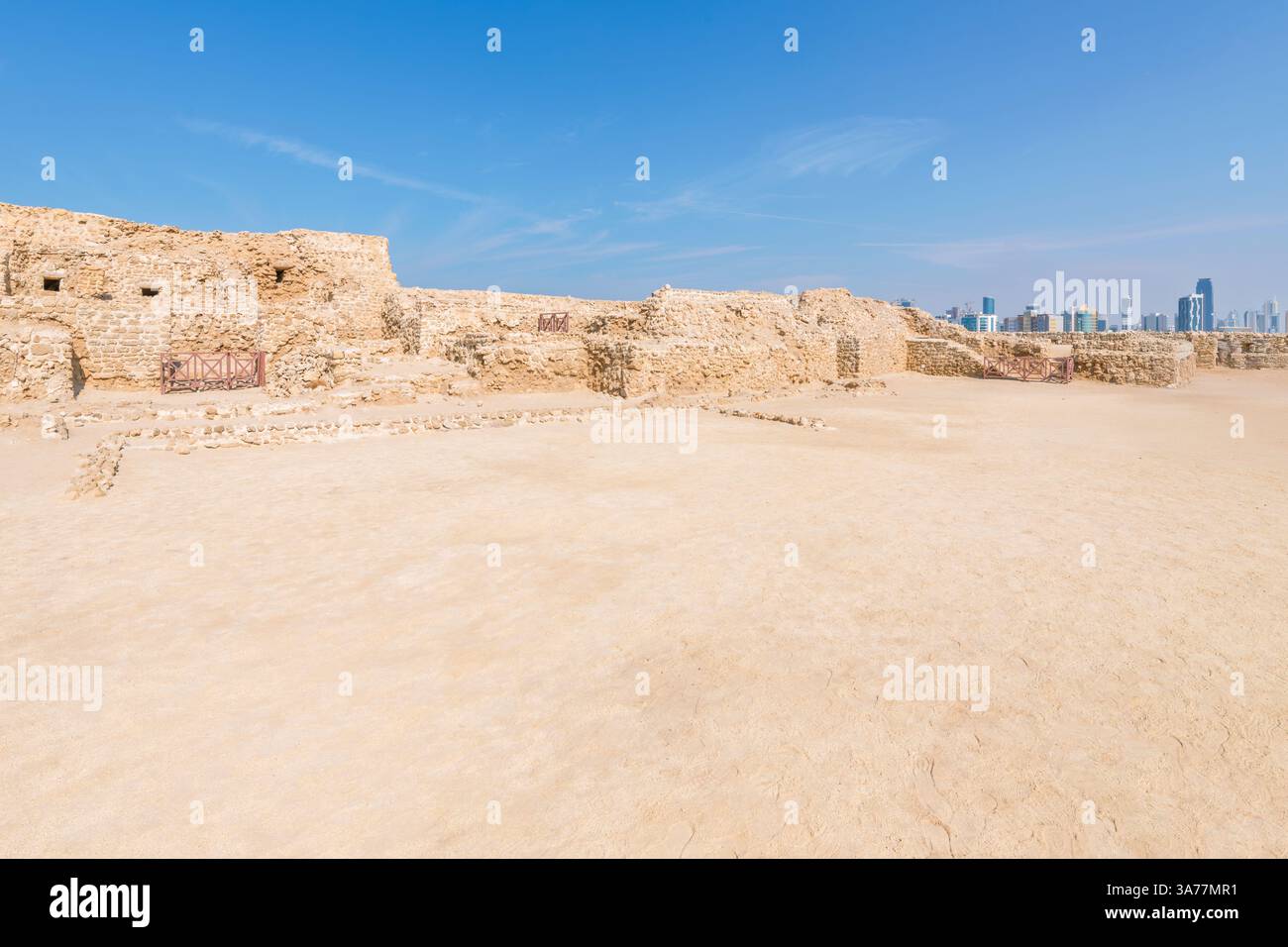 Das antike Qal'at al-Bahrain, auch bekannt als Bahrain Fort oder Portugiesisches Fort, mit der Skyline von Manama dahinter in Karbabad, Bahrain, Persischer Golf. Stockfoto