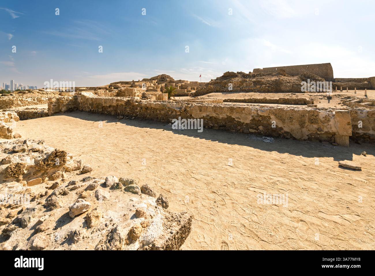 Das antike Qal'at al-Bahrain, auch bekannt als Bahrain Fort oder Portugiesisches Fort, mit der Skyline von Manama dahinter in Karbabad, Bahrain, Persischer Golf. Stockfoto