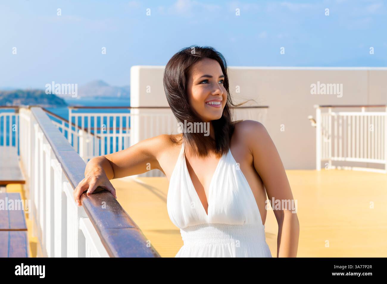 Eine hübsche junge brünette Frau in einem weißen Sonnenkleid lächelnd auf dem Oberdeck eines Kreuzfahrtschiffs im Mittelmeer. Stockfoto
