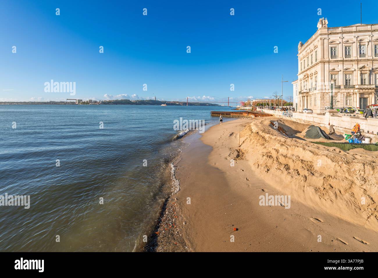 Der Sandstrand des Tejo am Kai Cais das Colunas vor dem Handelsplatz mit der Brücke vom 25. April im Zentrum von Lissabon, Portugal Stockfoto