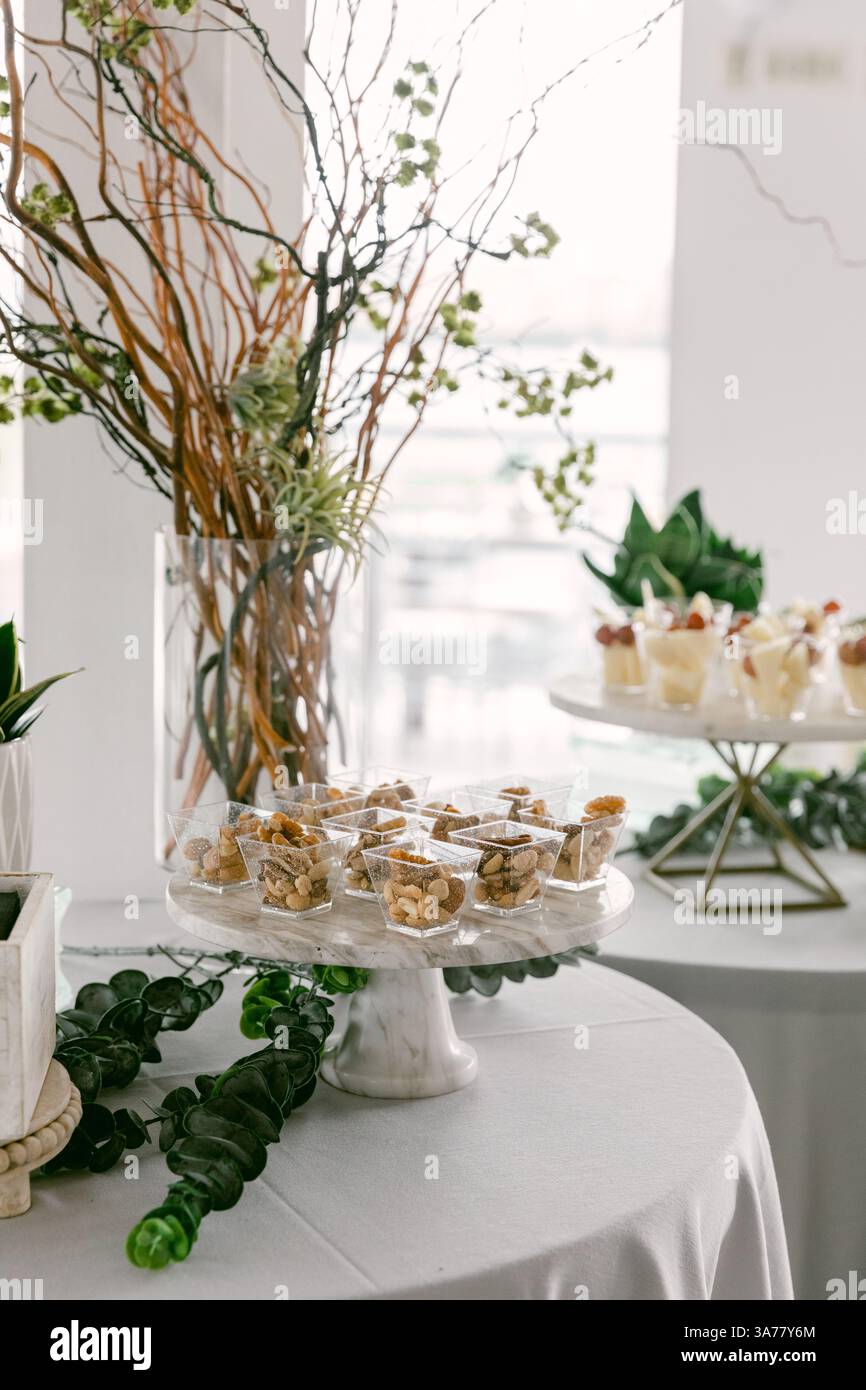 Delikates Gebäck und süße Köstlichkeiten an einem Stand mit üppigem Grün und Blumenakzenten in einem stilvollen Veranstaltungsort. Stockfoto