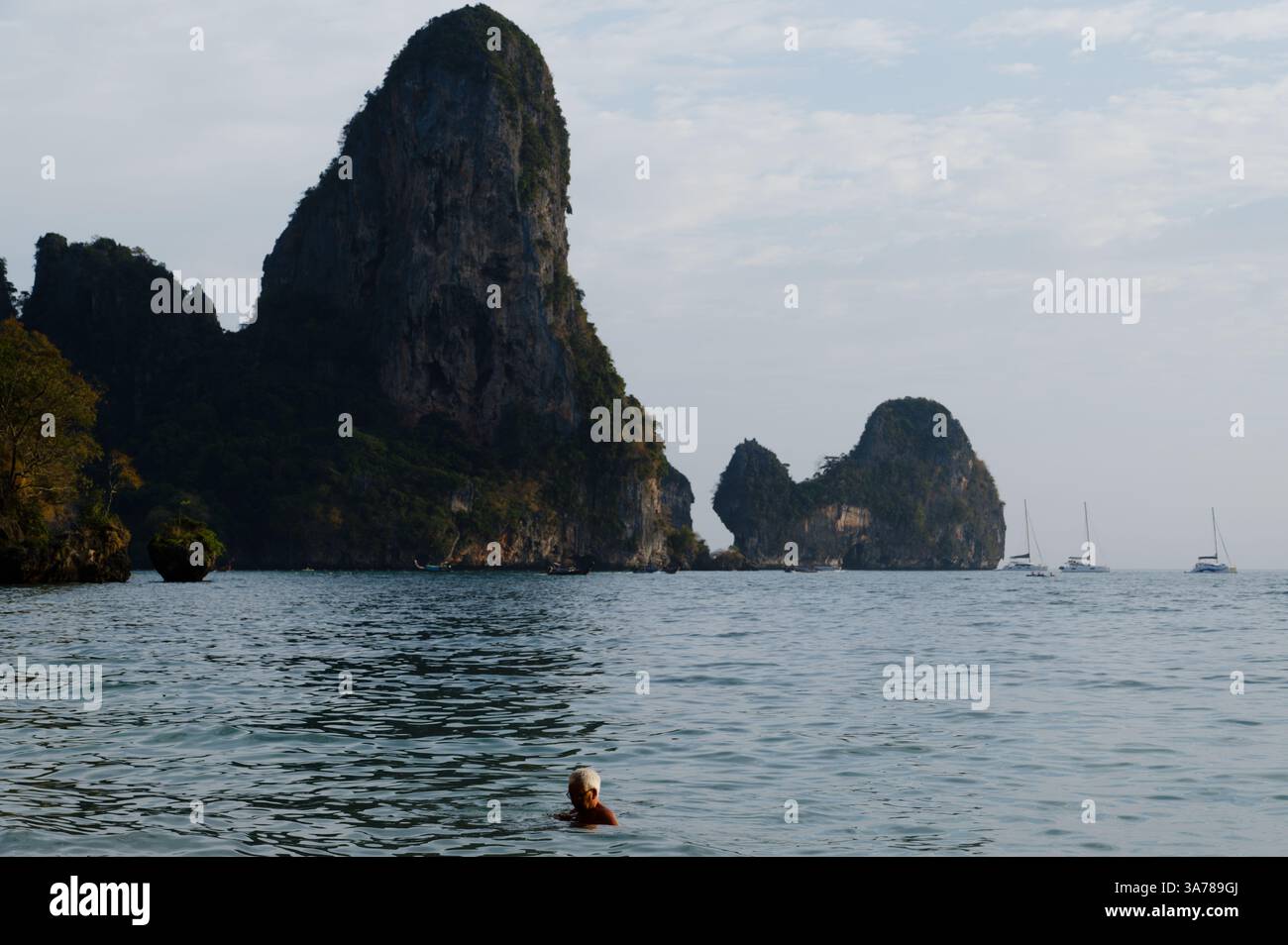 Reife Schwimmer schweben im ruhigen Wasser vor Tonsai Beach, umgeben von hohen Kalksteinklippen und weit entfernten, verankerten Segelbooten Stockfoto