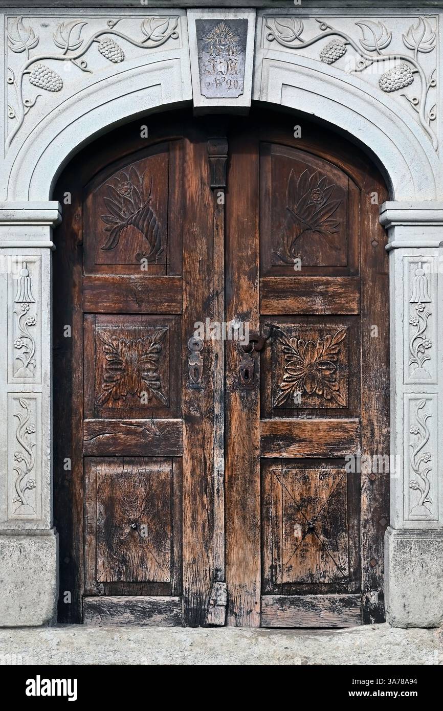 Verzierte antike Holztür mit geschnitzten Mustern in dekorativem Steinrahmen im Dorf Stara Fužina in der Nähe des Bohinj-Sees in den Julischen Alpen, Slowenien Stockfoto