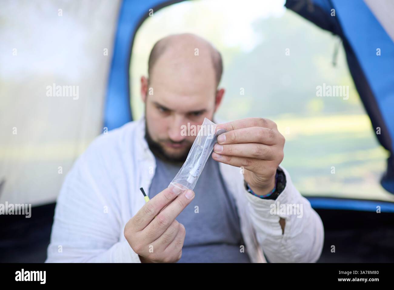 Reisender Mann, der Kleber aus seinem Gepäck zieht, um ein Loch im Netz seines Zeltes zu reparieren, indem er einen Flicken aufbaut. Selektiver Fokus auf Hände und Kopierraum. Stockfoto
