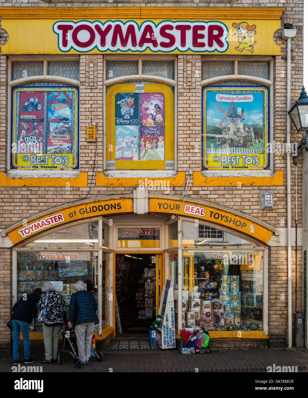 3 deutsche ältere weibliche Touristen schauen in das Fenster eines alten Spielwarengeschäfts Gliddons in Sidmouth, Devon, England. Stockfoto