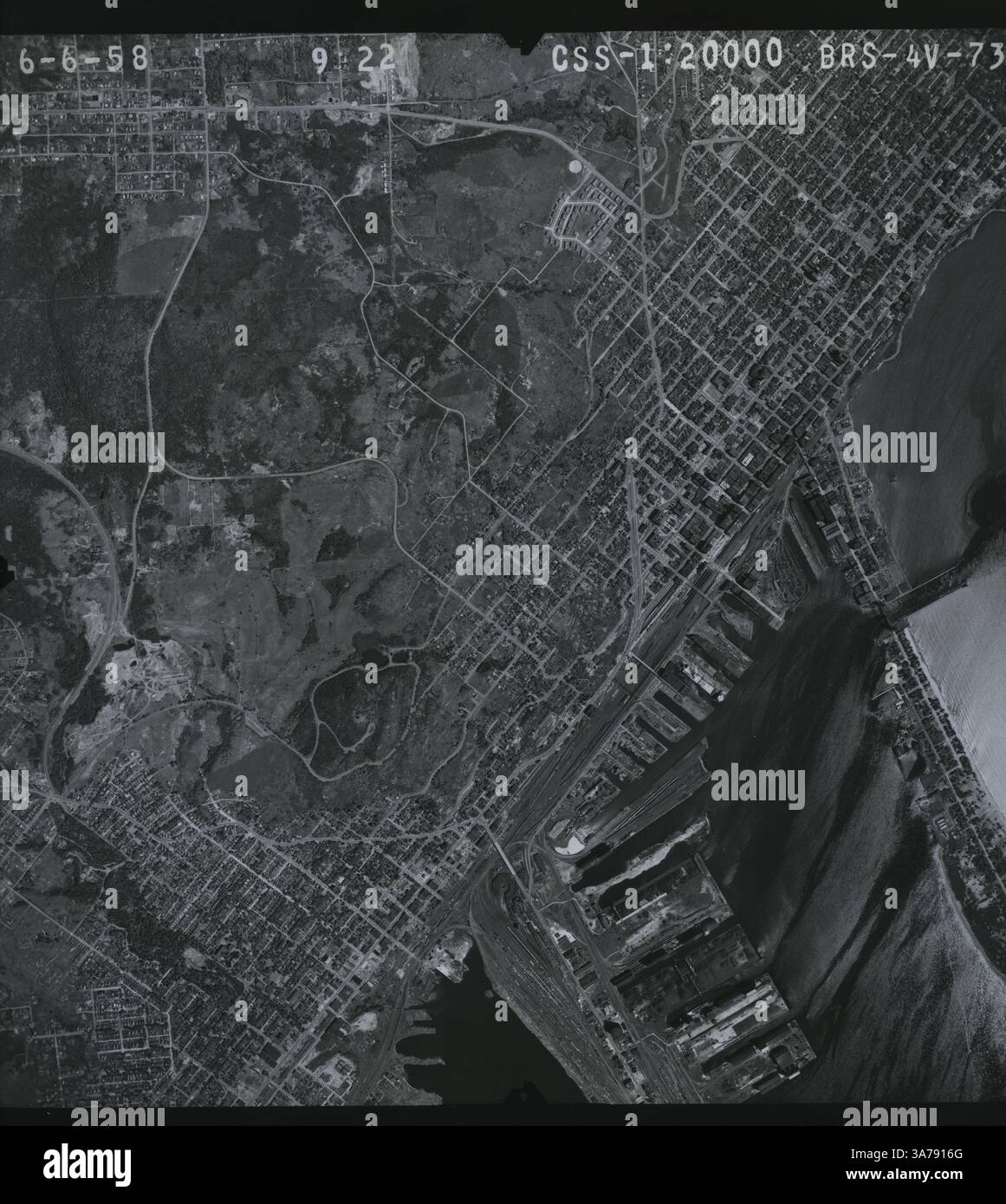 Luftaufnahme von Duluth, Minnesota, aufgenommen am 6. Juni 1958, zeigt das Straßengitter der Stadt, weitläufige Industriehäfen entlang des Lake Superior und die umliegenden Parks und Wohnviertel. Das Bild unterstreicht Duluths Rolle als wichtiger Schifffahrtsdrehkreuz im oberen Mittleren Westen in der Mitte des 20. Jahrhunderts. Stockfoto