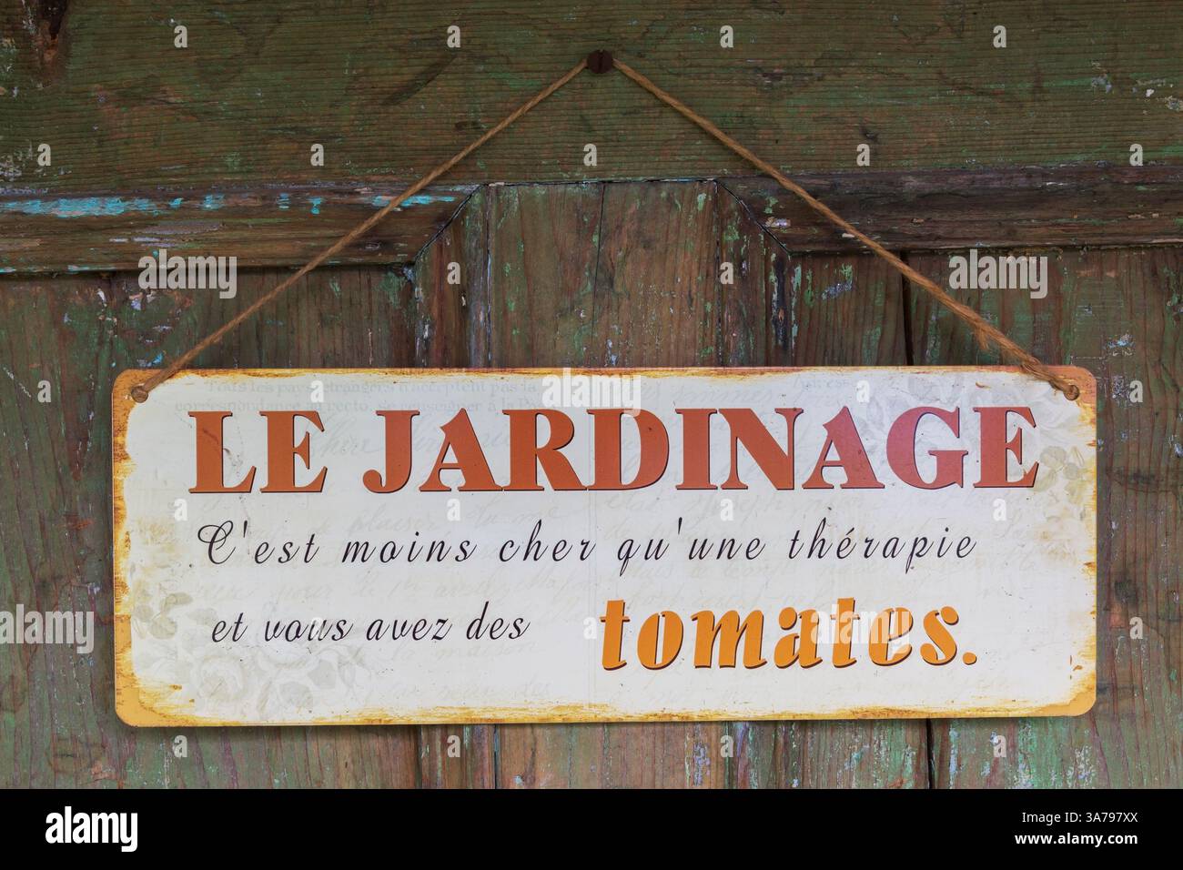 Das französische Le Jardinage-Schild hing an einer Tür mit Sprichwort, das besagt, dass Gartenarbeit weniger kostet als eine Therapie und man hat Tomaten. Stockfoto