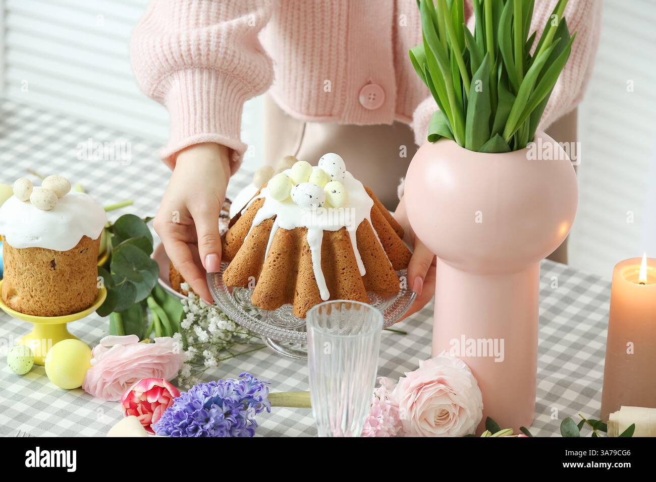 Frau, die Osterkuchen auf einem Tablett in der Nähe des Tischs hält, um die Osterfeier im Zimmer zu feiern. Nahaufnahme Stockfoto