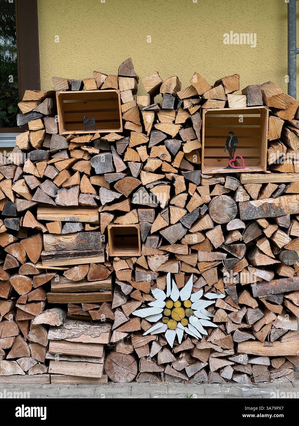 Ein dekorativer Holzhaufen vor dem Swiss Hotel Edelweiss mit einer Edelweiß-Blume aus bemalten Holzstämmen. - Smartphone-aufgenommenes Stockfoto