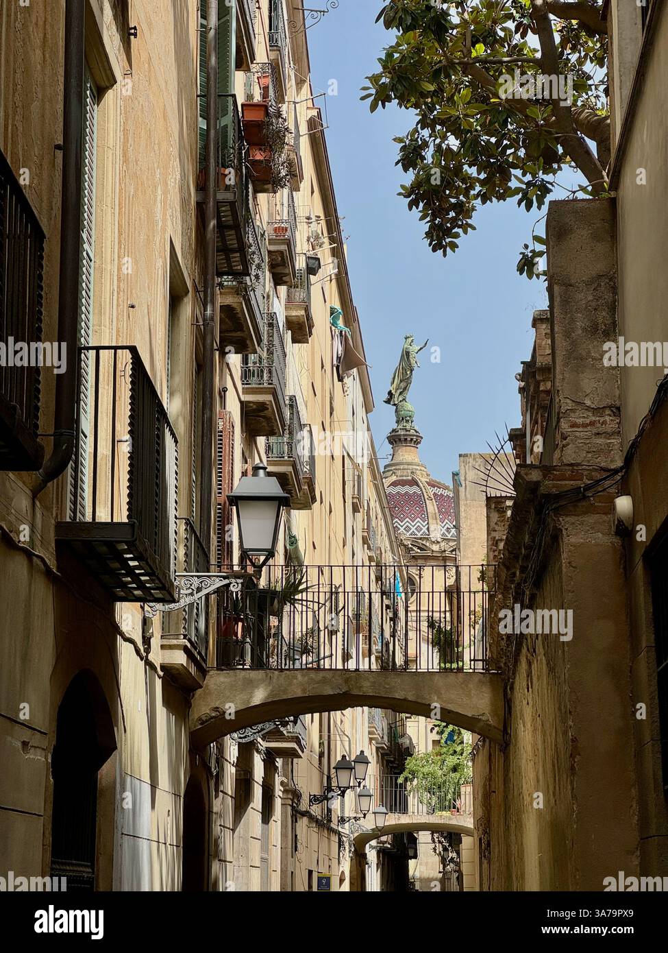 Der Blick entlang der Gasse Carrer de la Carabassa zur Statue unserer Lieben Frau auf der Kuppel der Basilika unserer Lieben Frau von Barmherzigkeit in Barcelona. - Smartphone-aufgenommenes Stockfoto