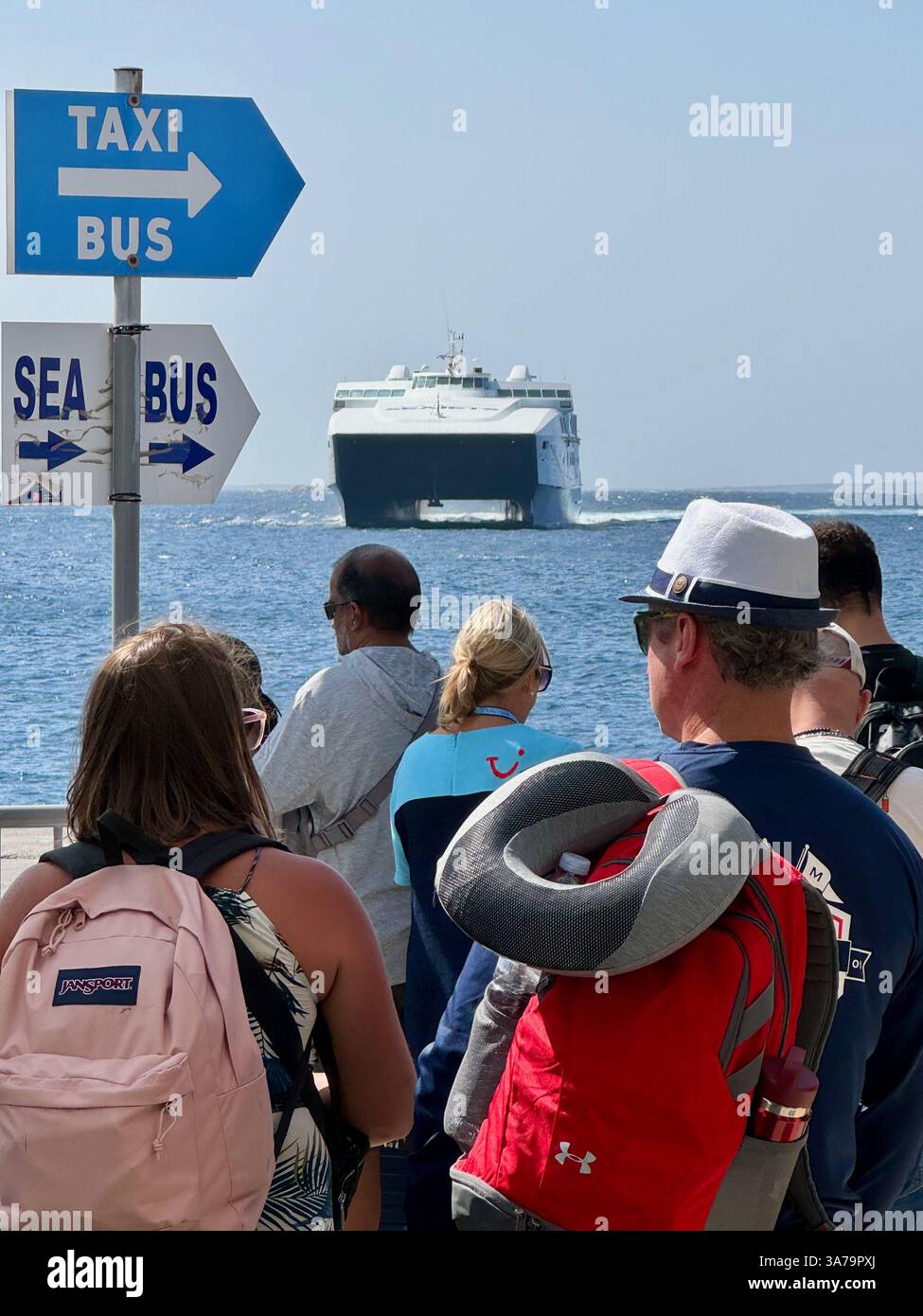 Touristen, die auf eine riesige Katamaran-Fähre im neuen Hafen auf Mykonos, Griechenland, warten. - Smartphone-aufgenommenes Stockfoto