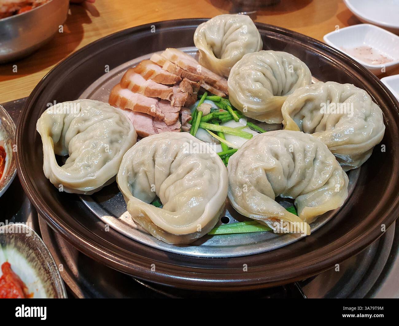 Köstliches koreanisches Gericht mit gedämpften Knödeln (wang mandu) und gekochtem Schweinebauch (bossam) auf einer Dampfschale. Eine klassische Kombination. Stockfoto