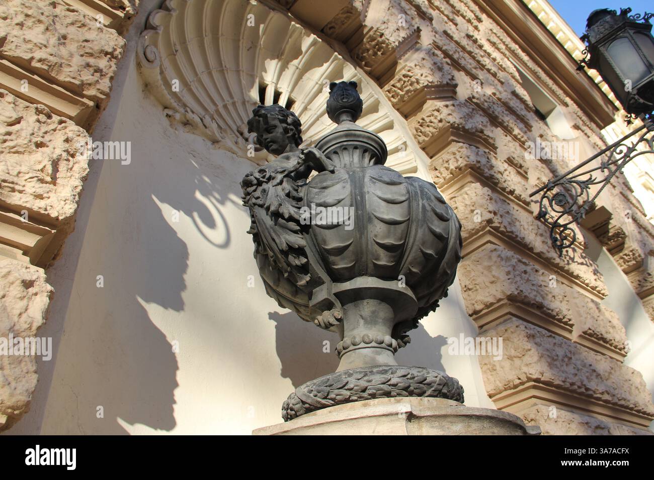 Klassische Steinskulptur eines Cherubs, der sich an eine verzierte dekorative Urne auf einer rustizierten Gebäudefassade in einer europäischen Stadtszene klammert. Stockfoto