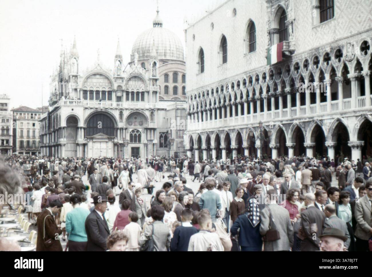 Der Markusplatz in Venedig wird von Menschenmassen bevölkert und bietet eine lebhafte Mischung aus Einheimischen und Touristen, die einen lebhaften Tag genießen. Aufgenommen im Juli 1965 auf 35-mm-Diafilm. Stockfoto