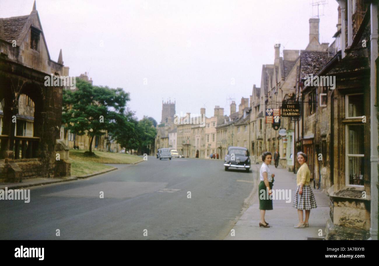 Eine bezaubernde Szene aus den 1960er Jahren, aufgenommen auf 35-mm-Diafilm, die die High Street in Chipping Campden, Gloucestershire, zeigt. Zwei Frauen stehen vor den Bantam Tea Rooms mit klassischen Steinhäusern, Oldtimern und einem entfernten Kirchturm, der den Ton dieser friedlichen Stadt in Cotswold bildet. Stockfoto