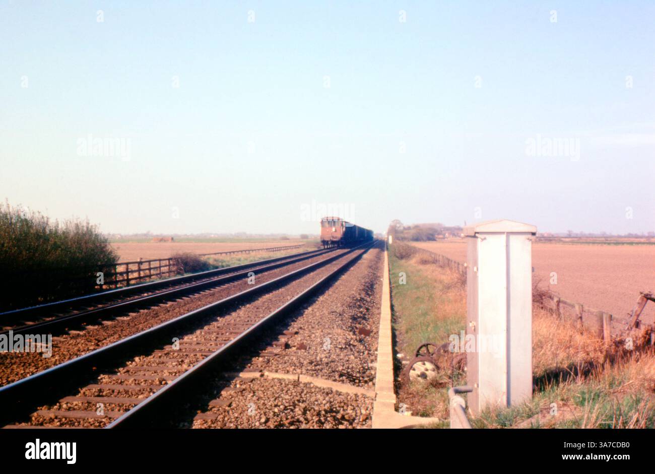 Ein alter Güterzug der British Rail fährt an einem klaren Tag in den 1960er Jahren durch die offene Landschaft Der einzelne Bremsträger am Heck deutet auf das Ende eines langen Güterzuges hin, typisch für den ländlichen Güterverkehr dieser Zeit. Stockfoto