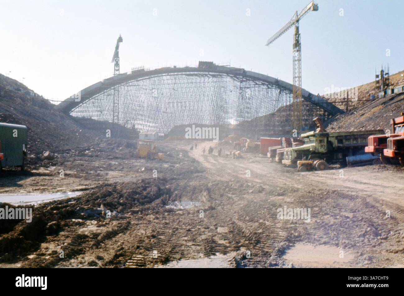 Dieses Foto vom April 1969 zeigt den Bau der Scammonden Bridge, Teil der Autobahn M62 in West Yorkshire. Die Szene dominiert das massive Zentriergerüst, das den Betonbogen der Brücke während des Baus stützt. Das umliegende matschige Gelände, die Maschinen und die Kräne verdeutlichen den Umfang und die Komplexität dieser technischen Meisterleistung, die über dem Scammonden Dam in den Pennines gebaut wurde. Stockfoto