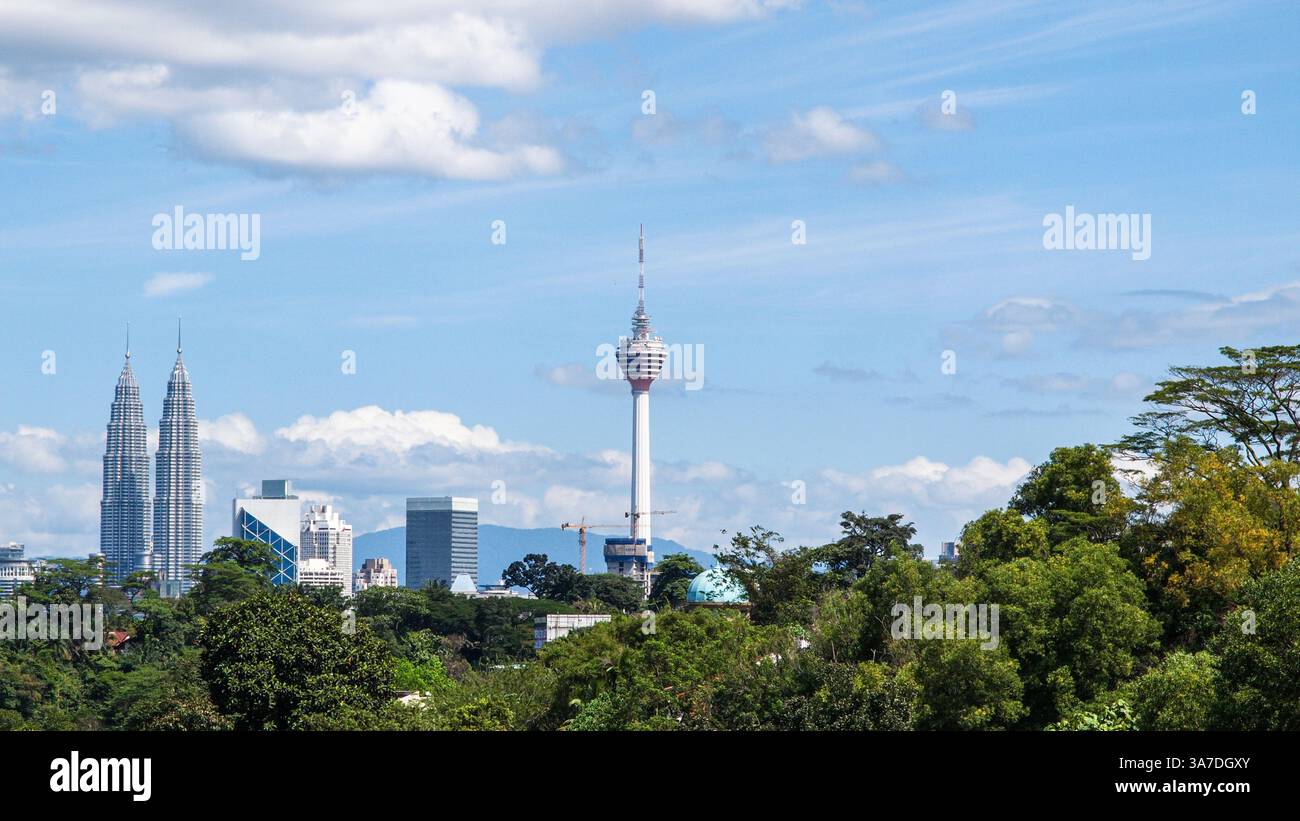Städtische Landschaft der Petronas Twin Towers und des Menara Kuala Lumpur Tower mit einigen Bäumen, blauem Himmel und Wolken. Stockfoto