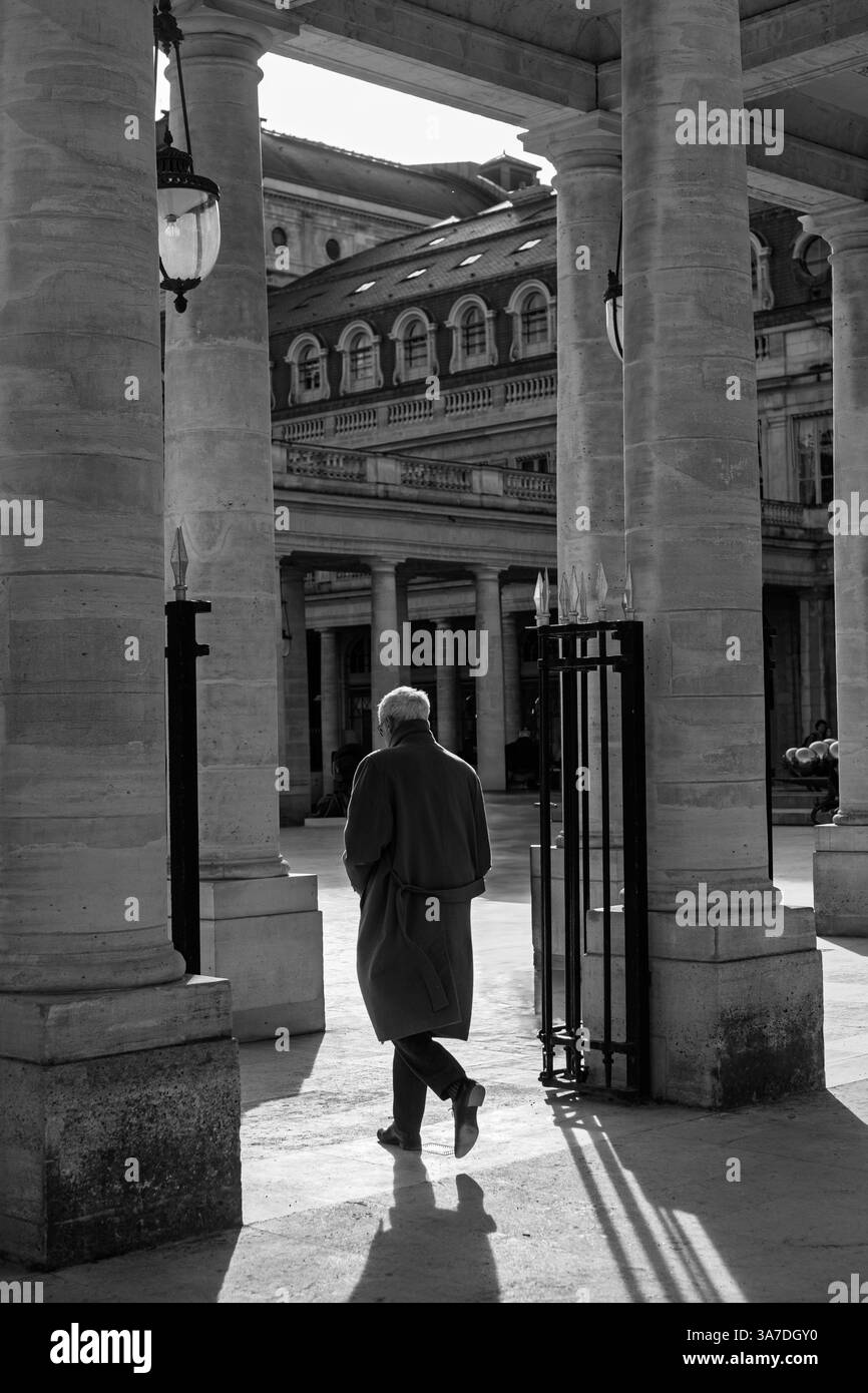 Älterer Mann, der durch die elegante Kolonnade des Palais Royal in Paris geht, in zeitlosem Schwarz-weiß. Stockfoto