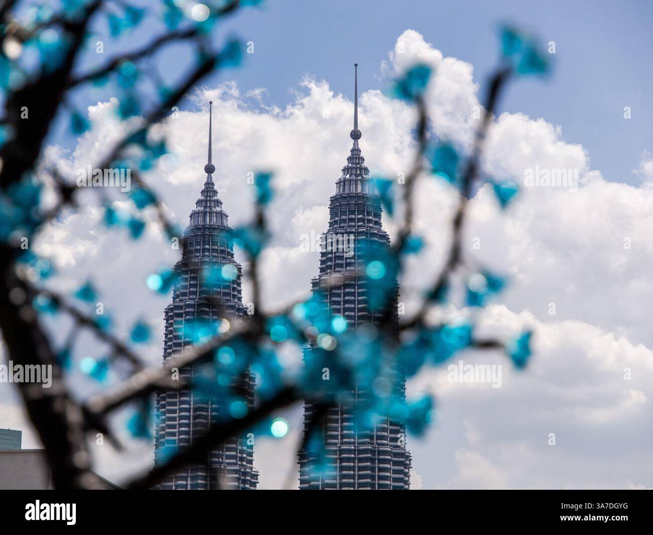 Petronas Twin Tower hinter einem unscharfen blauen Kristallglasbaum und Blumen mit weißen Wolken und blauem Himmel. Stockfoto Petronas Twin Tower hinter einem unscharfen blauen Kristallglasbaum und Blumen mit weißen Wolken und blauem Himmel. Stockfoto