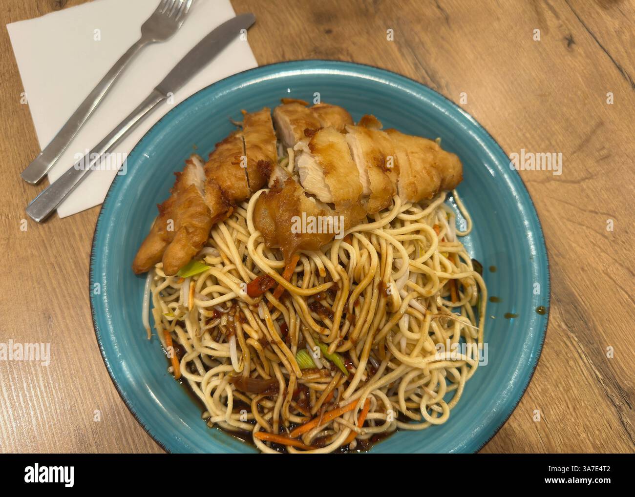 Asiatische Nudelpfanne mit knusprigem Hähnchen , Deutschland, Rheinland-Pfalz, 27.03.2025, frisch gebratene Nudeln mit Gemüse, Sojasauce und knusprigem Hähnchenfilet serviert auf blauem Teller. *** Asiatische Nudelpfanne mit knusprigem Huhn, Deutschland, Rheinland-Pfalz, 27 03 2025, frisch gebratene Nudeln mit Gemüse, Sojasauce und knusprigem Hähnchenfilet auf blauem Teller serviert Stockfoto