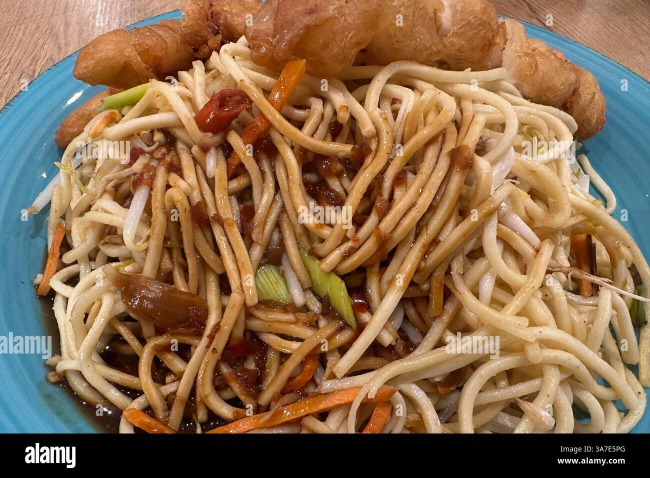 Asiatische Nudelpfanne mit knusprigem Hähnchen , Deutschland, Rheinland-Pfalz, 27.03.2025, frisch gebratene Nudeln mit Gemüse, Sojasauce und knusprigem Hähnchenfilet serviert auf blauem Teller. *** Asiatische Nudelpfanne mit knusprigem Huhn, Deutschland, Rheinland-Pfalz, 27 03 2025, frisch gebratene Nudeln mit Gemüse, Sojasauce und knusprigem Hähnchenfilet auf blauem Teller serviert Stockfoto