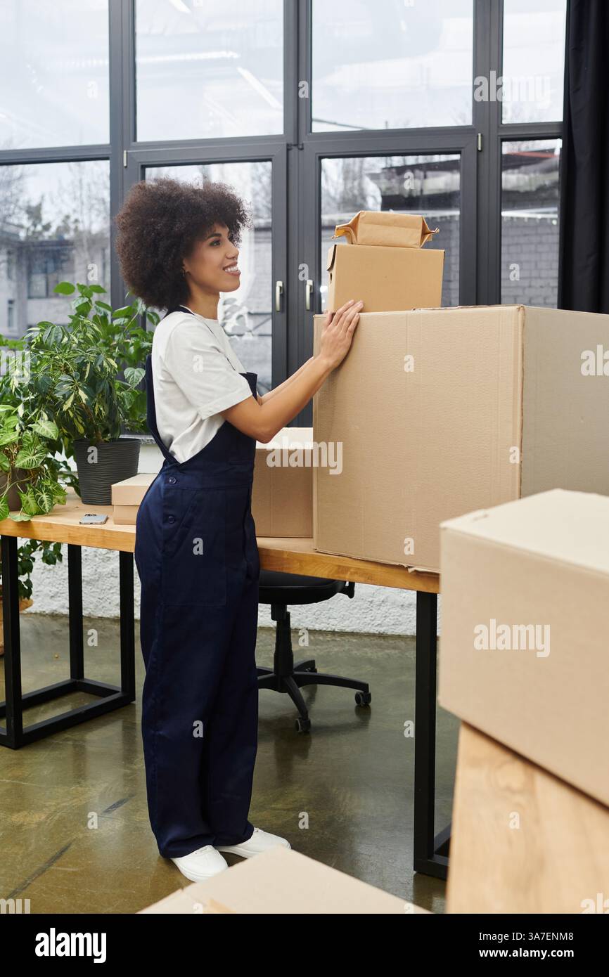Eine Frau organisiert Kisten in einem modernen Büro, während sie für einen Umzug packt, umgeben von Pflanzen. Stockfoto
