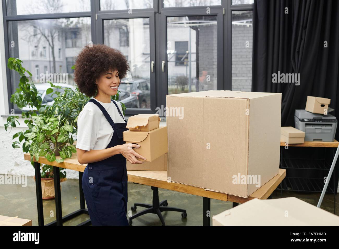 Eine Frau packt Kisten in einem eleganten, von Grün umgebenen Arbeitsbereich und bereitet sich auf einen Umzug vor. Stockfoto