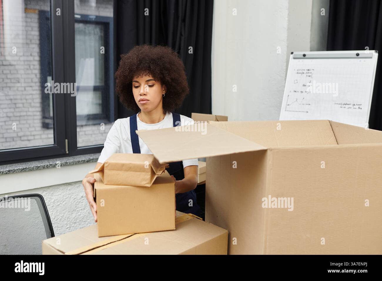 Eine Frau packt sorgfältig Kisten und bereitet sich auf einen modernen Umzugsprozess mit Fokus vor. Stockfoto