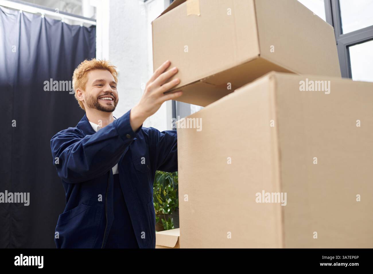 Ein fröhlicher Arbeiter stapelt während des Umzugs sorgfältig Kartons in einem modernen Büro. Stockfoto