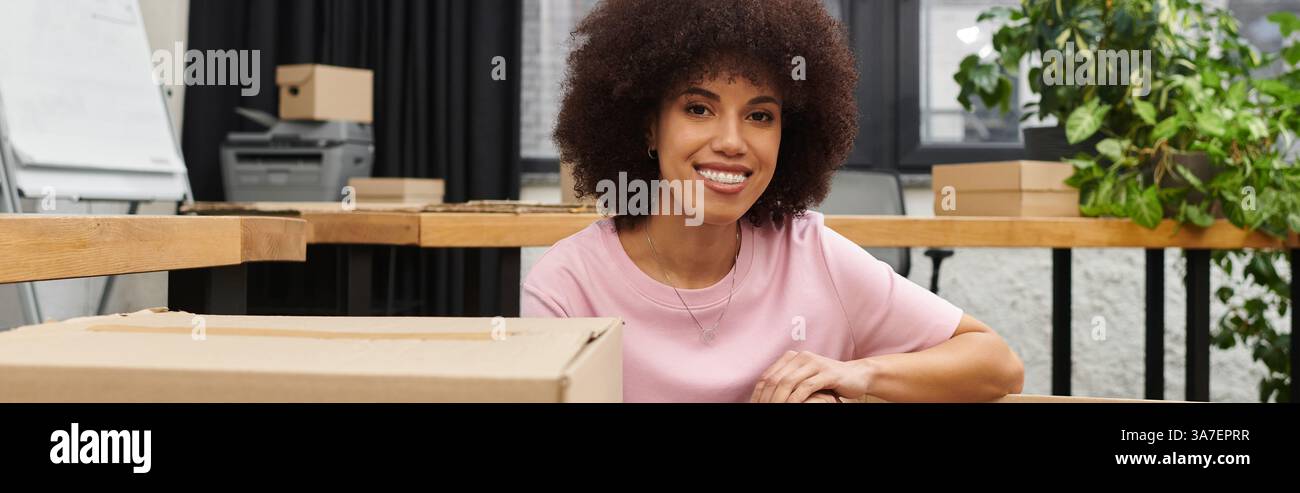 Eine lächelnde junge Frau mag es, an einem modernen Arbeitsplatz Kisten zu packen und auszupacken. Stockfoto