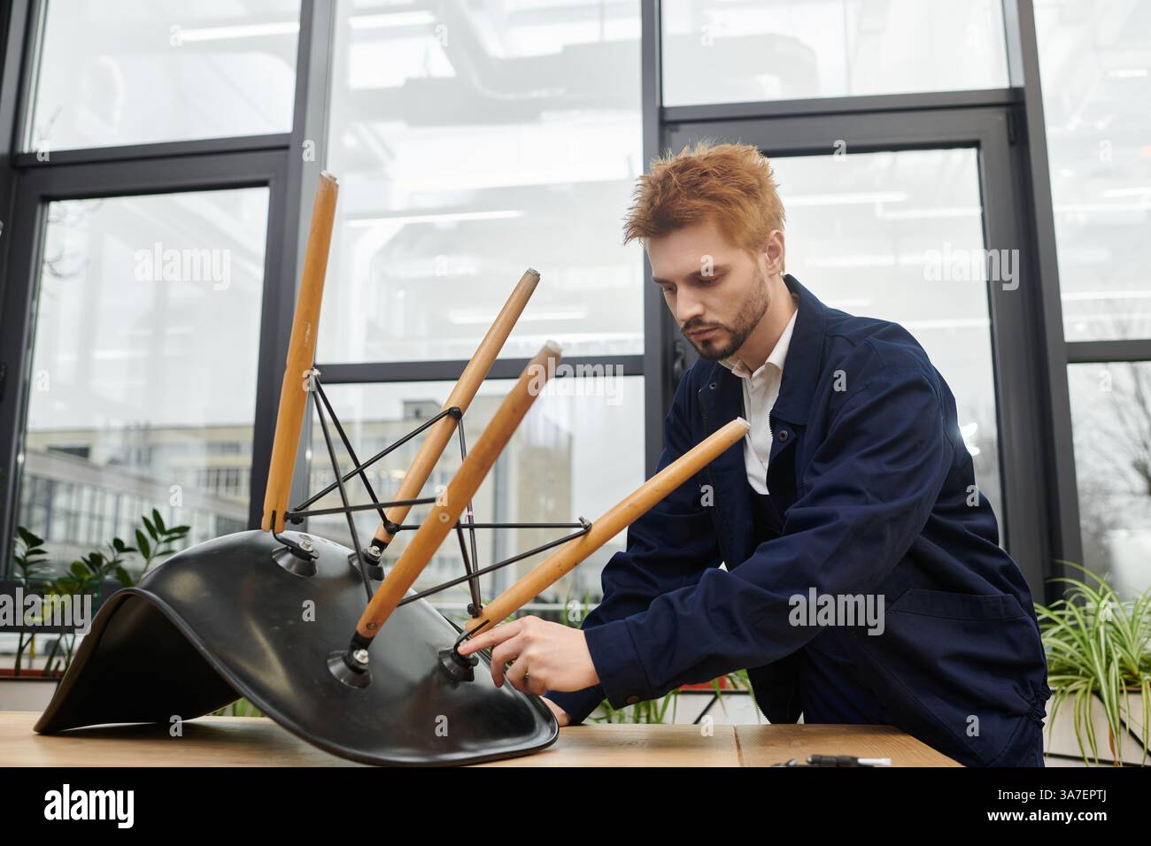 Ein junger Mann zerlegt vorsichtig einen Stuhl, während er sich auf eine Arbeitsumgebung vorbereitet. Stockfoto