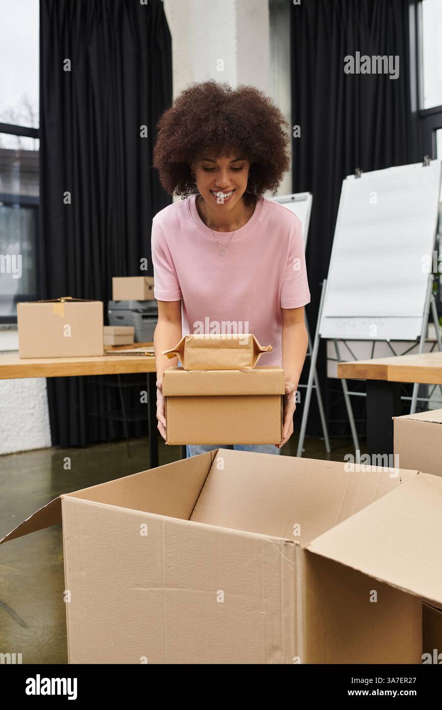 Eine Frau lächelt und hebt eine Kiste in einem modernen Büro an. Stockfoto