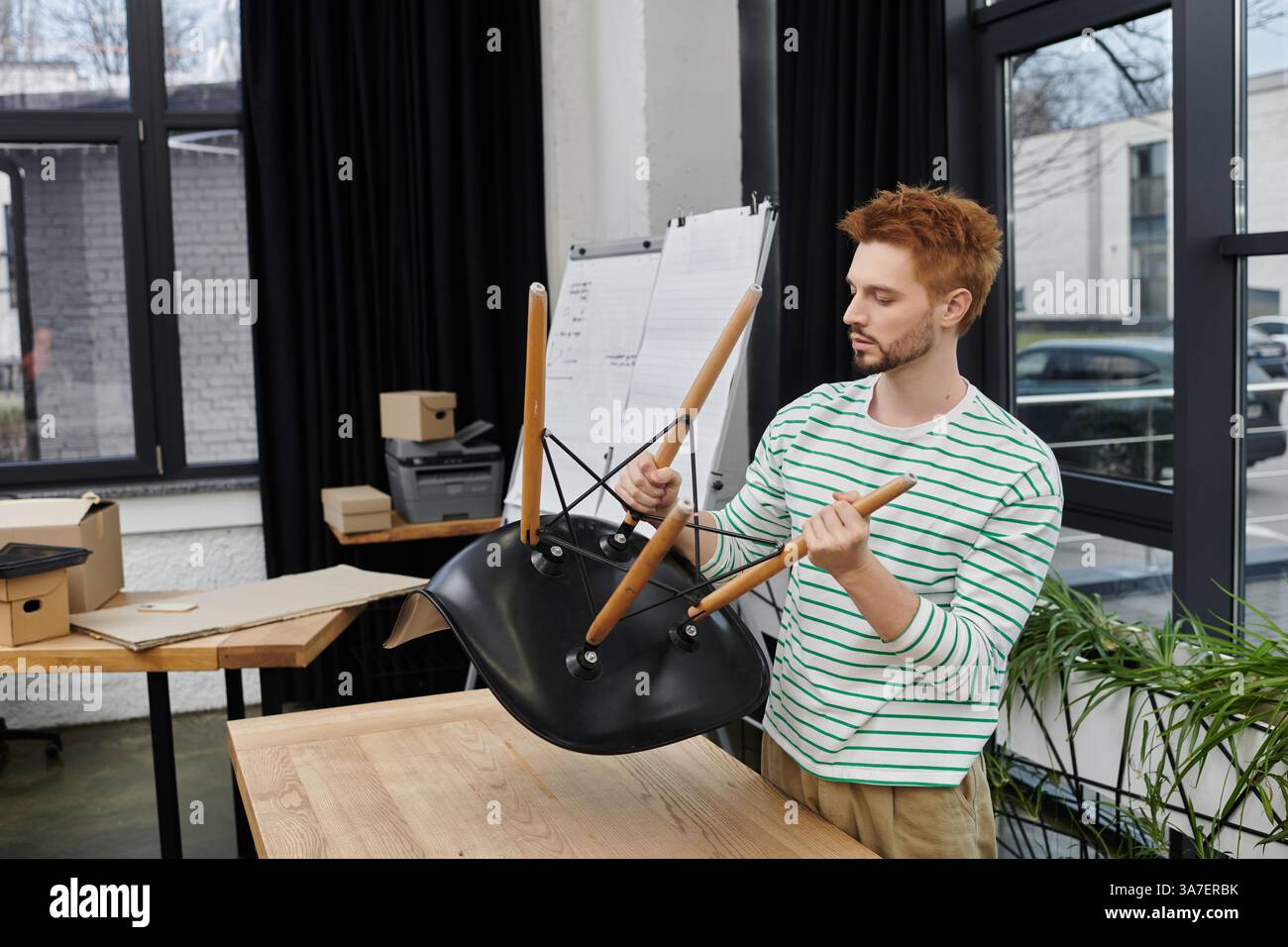 Ein Mann baut fachmännisch einen Stuhl in einem modernen Büro zusammen, während er sich auf den Umzug vorbereitet. Stockfoto