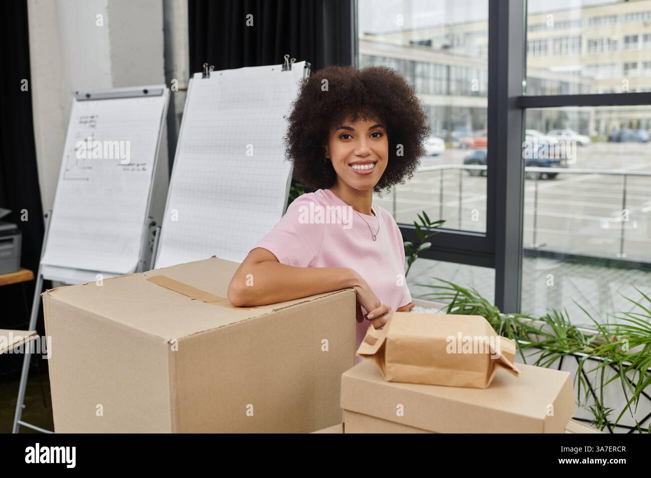 Eine Frau packt gerne Kartons in einem lebendigen und modernen Bürobereich. Stockfoto
