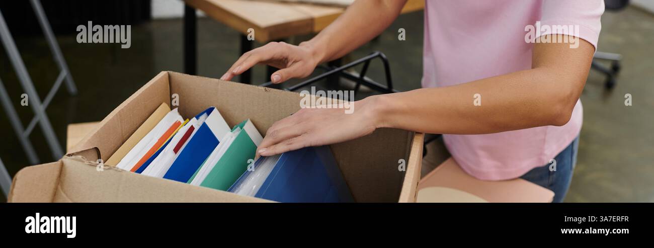 Eine Person sortiert in einem modernen Büro eine Box mit farbigen Ordnern und Büchern. Stockfoto