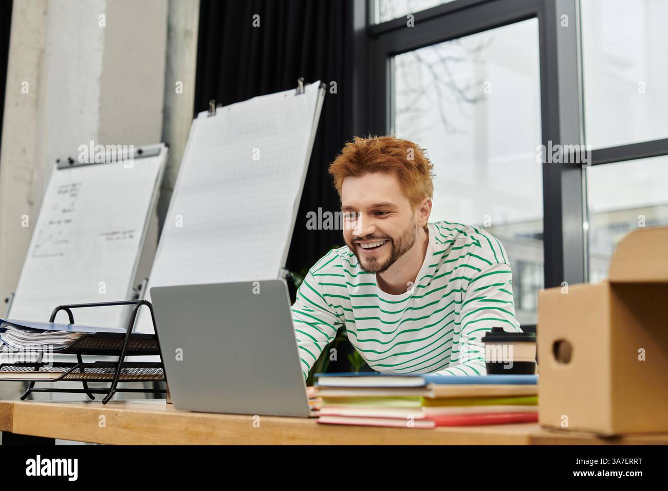 Ein junger Mann packt und packt aus, umgeben von beweglichen Vorräten in einem Heimbüro. Stockfoto