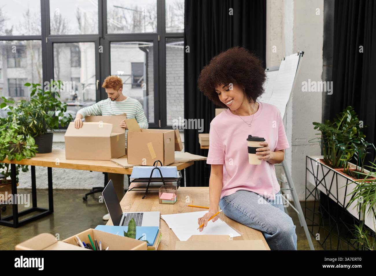 Zwei Personen packen Kisten und organisieren ihren eleganten Arbeitsplatz und genießen den Prozess gemeinsam. Stockfoto