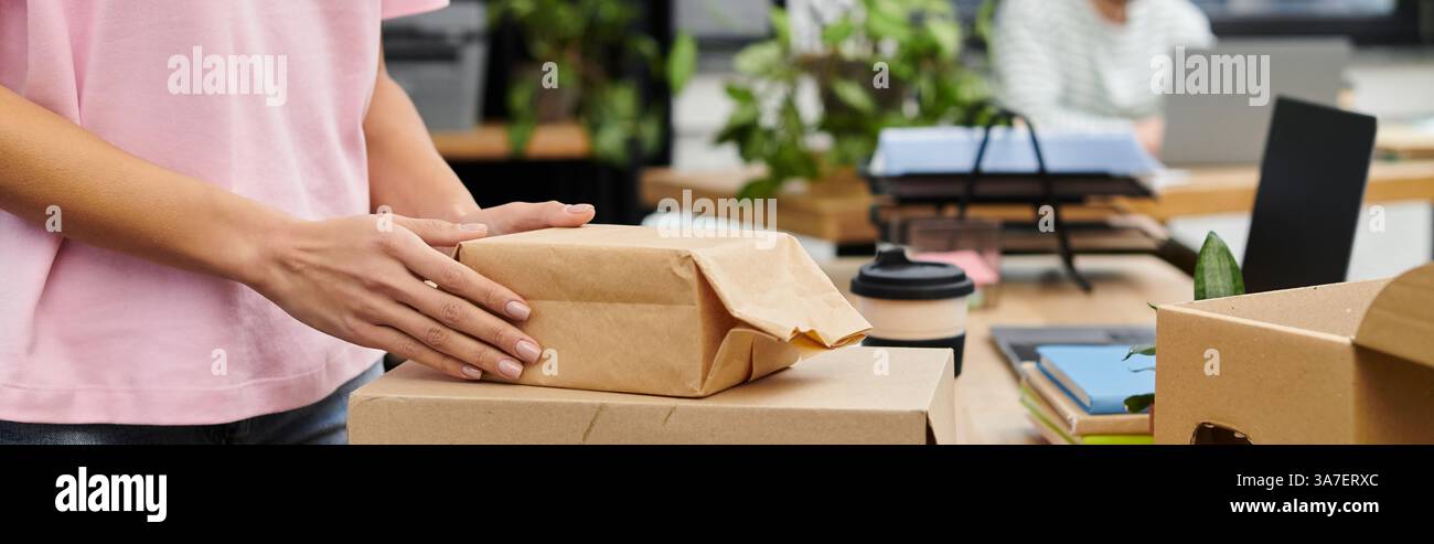 Die Hände wickeln ein kleines Paket, während der Arbeitsbereich vor Aktivität strotzt und Pflanzen die Tische zieren. Stockfoto