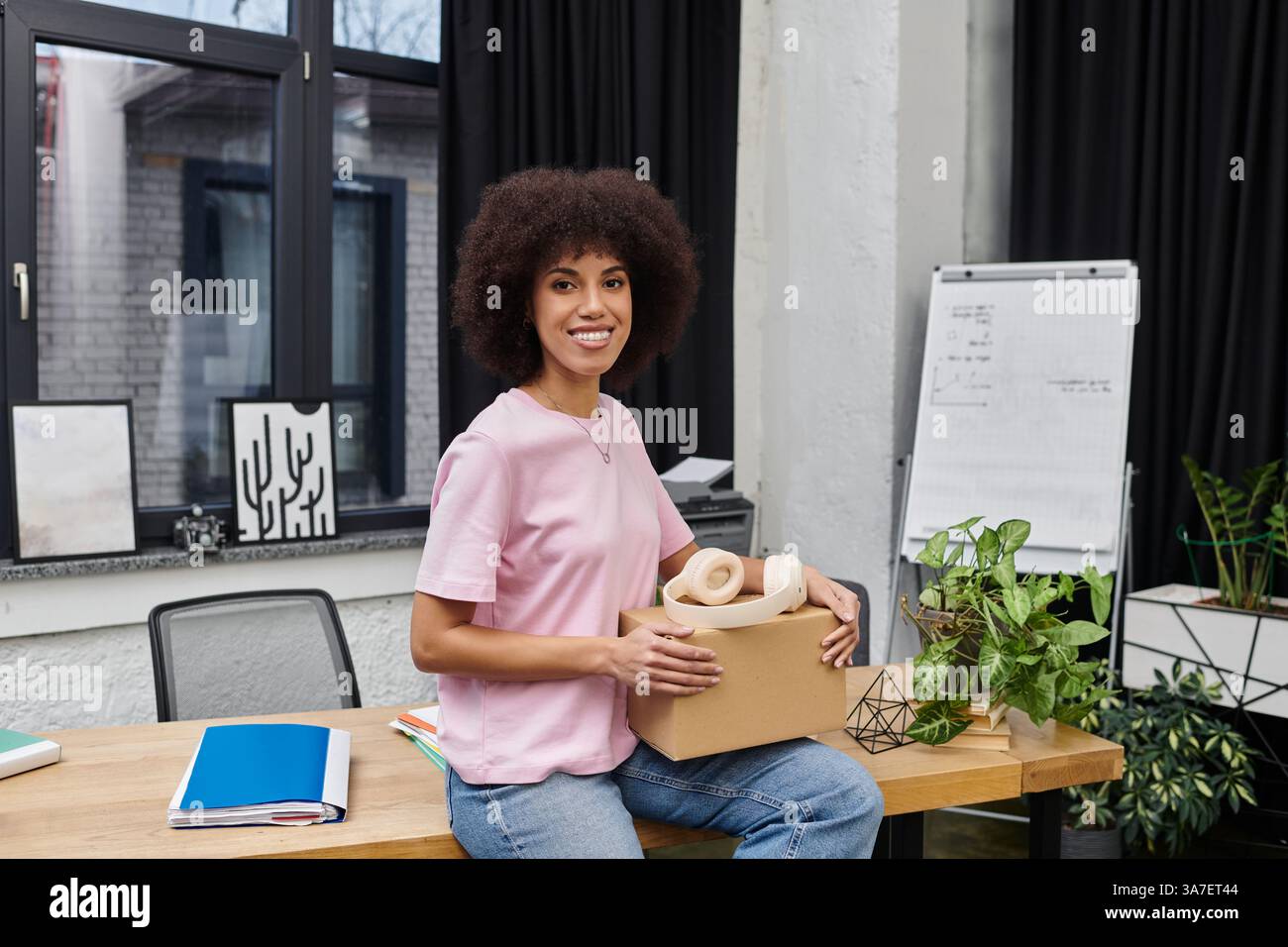 Eine fröhliche Frau hält eine Kiste, begeistert davon, sich in einer modernen Umgebung zu bewegen. Stockfoto
