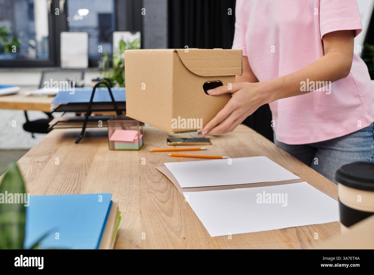 Eine Frau packt eine Kiste in ein helles, modernes Büro und bereitet sich auf einen Umzug vor. Stockfoto