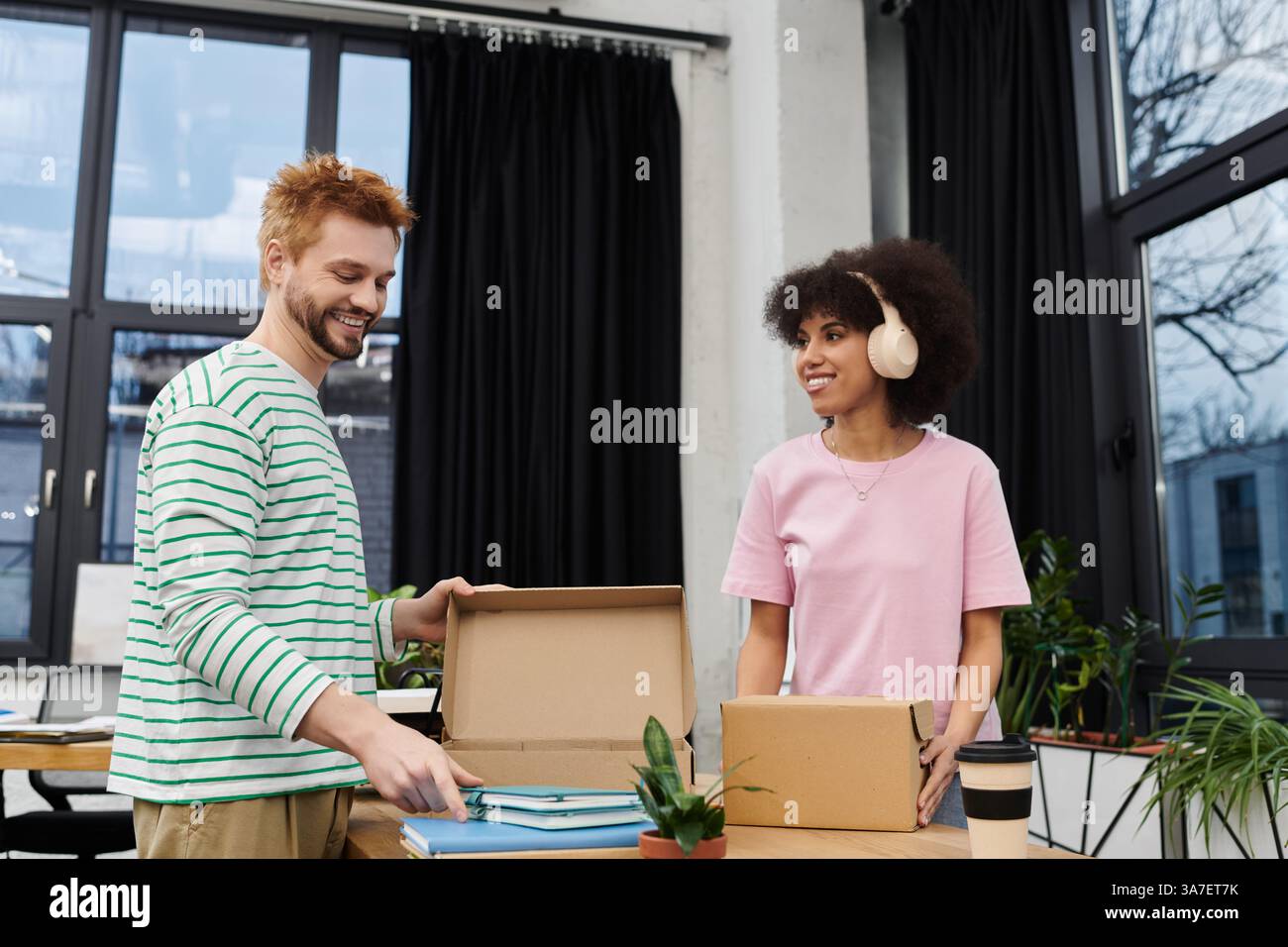 Zwei Freunde packen und auspacken gerne Kartons in einem hellen, modernen Arbeitsbereich. Stockfoto