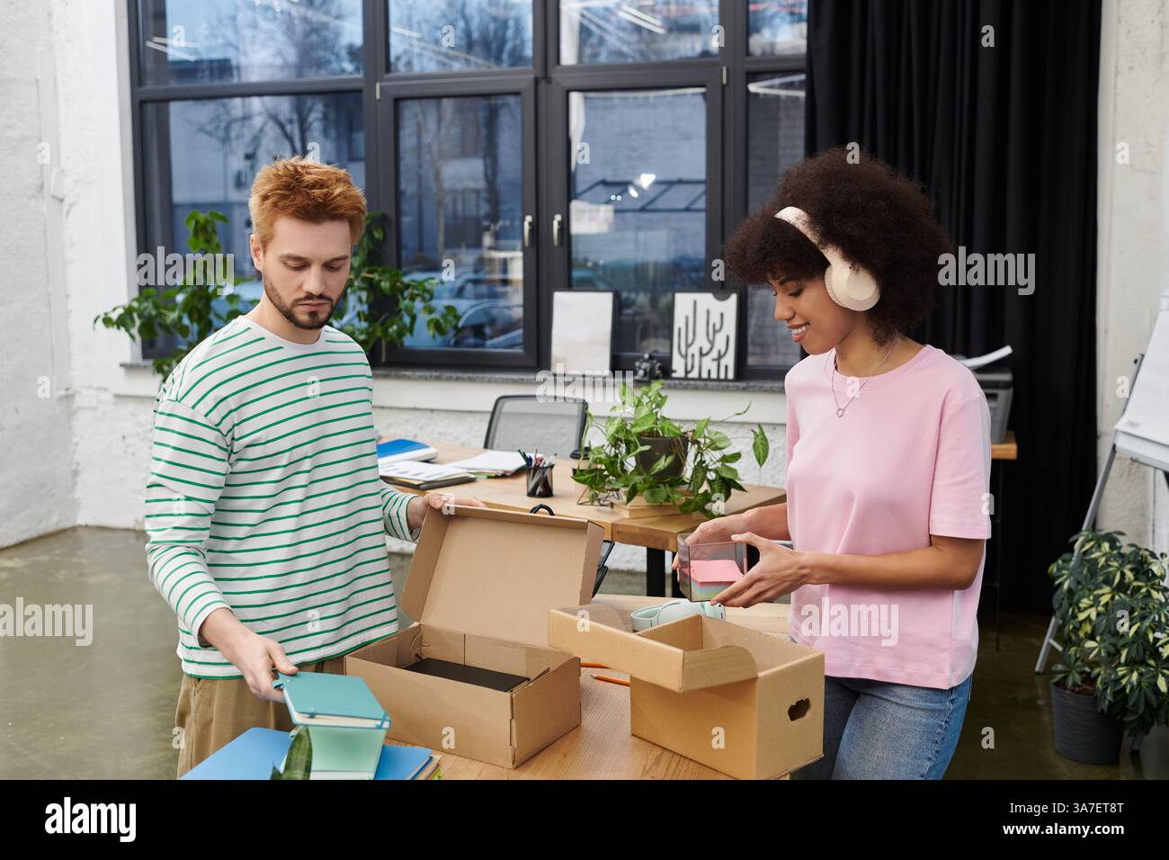 Zwei Personen packen und auspacken Kartons in einem modernen, grünen Bürobereich. Stockfoto