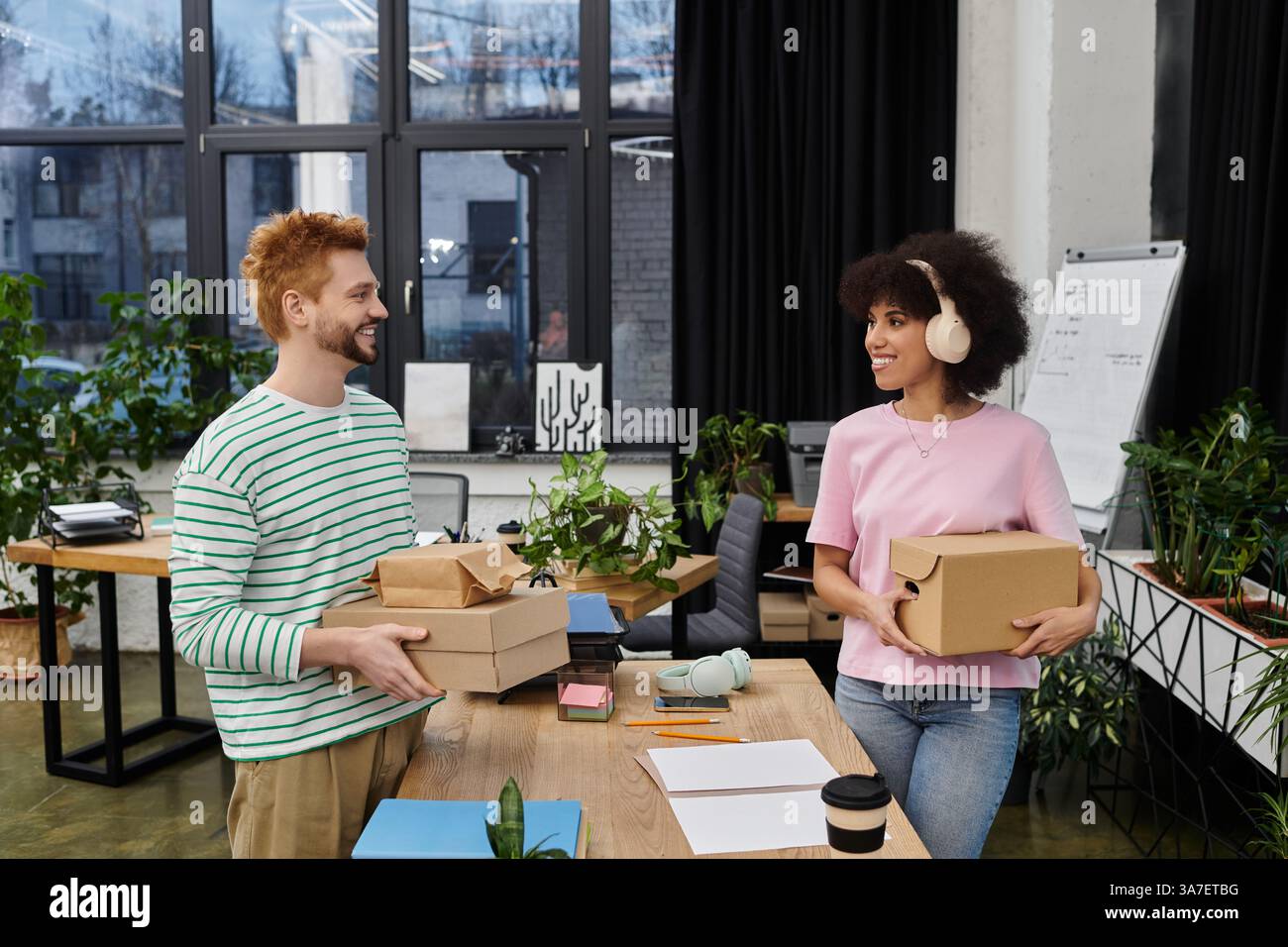 Zwei Personen verpacken gerne Kartons in einem hellen, grünen Arbeitsbereich. Stockfoto
