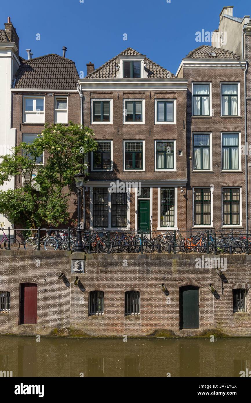 Vorderansicht des Oudegracht-Kanals mit Wand und Türen für den Eingang zum Untergeschoss. Ein Stahlzaun mit Fahrrädern und Ziegelhäusern an einem sonnigen Tag A Stockfoto