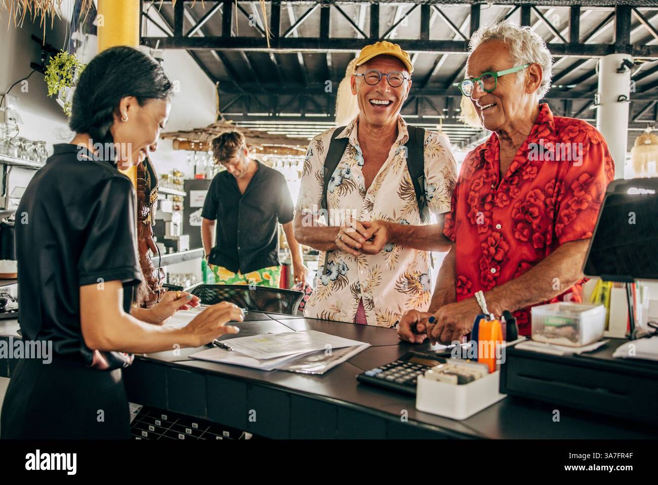 Glückliches älteres schwules Paar, das mit der Rezeptionistin beim Einchecken in der Ferienwohnung sprach Stockfoto