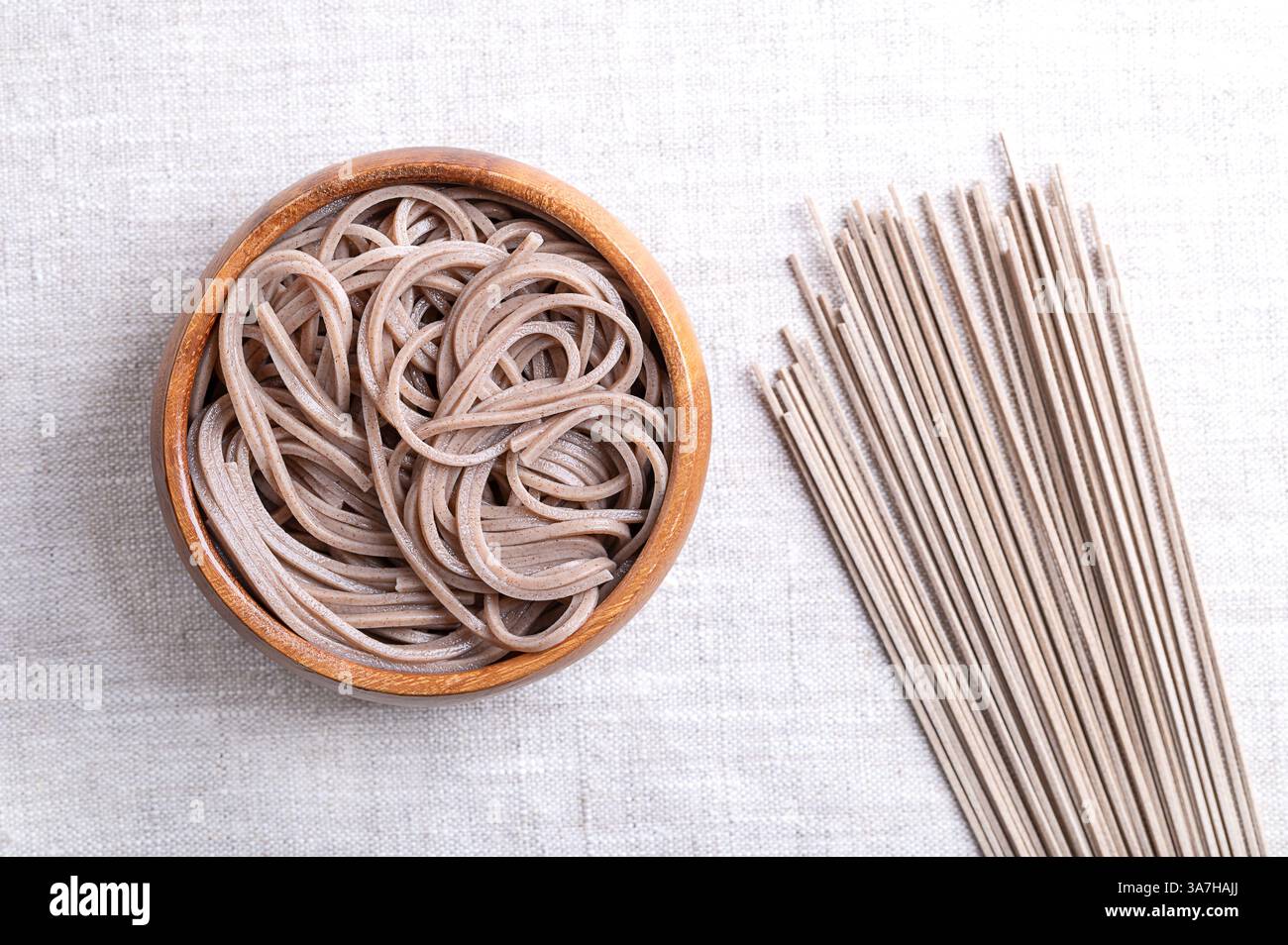 Gekühlte und gekochte Soba-Nudeln in einer Holzschale auf Leinenstoff. Dünne japanische Nudeln, hauptsächlich aus Buchweizenmehl hergestellt. Stockfoto